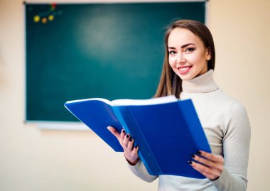 Sınıftaki genç ve güzel öğretmen. Öğretmen, okul ya da üniversite sınıfında klasör tutuyor. Eğitim. Görev.