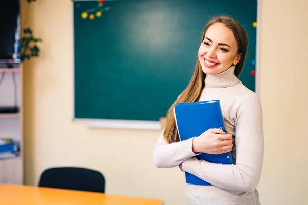 Teacher giving lesson to students in classroom. Teacher holds folder in classroom of school or university. Education, school, learning. Teacher in classroom. Smiling girl student or woman teacher. — Stock Photo, Image