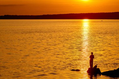 Gün batımı saatinde iskelede balıkçı. Nehirde güzel gün batımı ve balıkçılık çubukları ile adam.