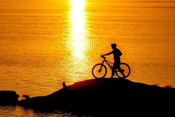 Silhueta de desportista a andar de bicicleta na praia. Céu nublado colorido ao pôr-do-sol no fundo . — Fotografia de Stock