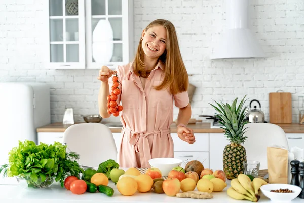 Menina de pé na cozinha segurando um monte de tomate vermelho em suas mãos. Dona de casa tomando ingredientes frescos para salada de legumes . — Fotografia de Stock