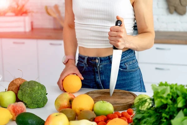 Mujer joven deportiva está cortando naranja fresca para el jugo de frutas en la cocina. Nutrición saludable — Foto de Stock