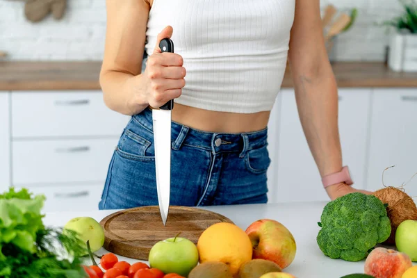 Mujer joven sosteniendo cuchillo mientras cocina ensalada de verduras frescas en el interior de la cocina en casa. Nutrición saludable — Foto de Stock