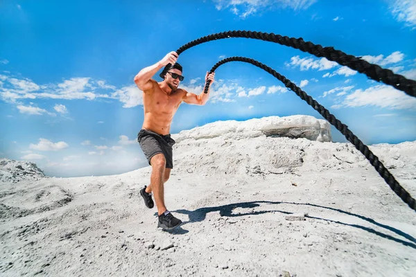 Savaş halatlarıyla çalışan kaslı adam. Atletik genç adam savaş halatları açık havada çalışıyor. Spora uygun egzersiz.