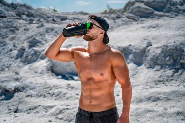 Vücut geliştirici egzersizden sonra dinleniyor ve protein içeceği içiyor. Açık hava sporu kavramı.