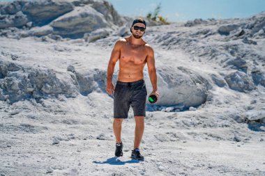 Elinde bir şişe suyla dağdaki yakışıklı, yarı çıplak vücutçunun portresi..