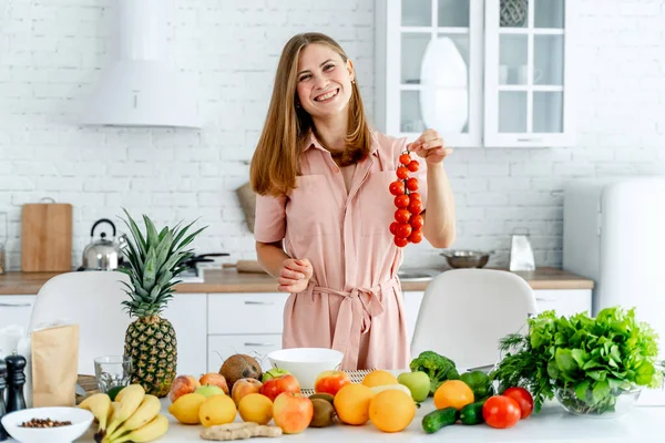 Mulher na cozinha pronta para preparar a refeição com legumes e frutas. A mulher está a segurar tomates. Fundo da cozinha. Comida saudável. Vegans. Vegeteriano. Banca de tomates . — Fotografia de Stock