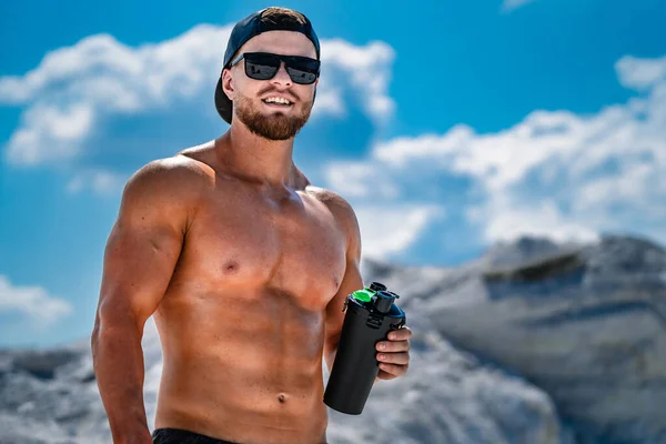 Retrato de um homem fisiculturista meio bonito em uma montanha com uma garrafa de água . — Fotografia de Stock