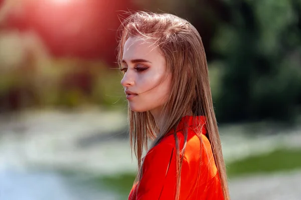 Retrato de uma bela jovem mulher em vermelho, vestido laranja. Vista para o parque. Vista do lago fundo borrado. Cabelo comprido. Bela maquilhagem. Fotocaça profissional. Fechar. . — Fotografia de Stock