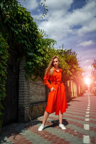 Φωτογραφία μιας ελκυστικής γυναίκας που φοράει κόκκινο φόρεμα σε φόντο δρόμου. Μακριά μαλλιά. Πορτρέτο ενός όμορφου κοριτσιού. Νεαρή γυναικεία φωτογράφηση. — Φωτογραφία Αρχείου