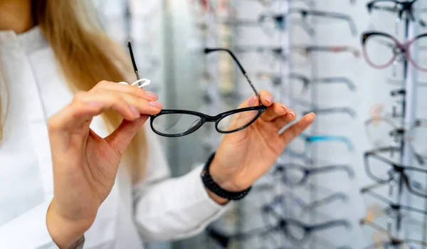 Fila di occhiali a un ottico. Negozio di occhiali. Stare con gli occhiali nel negozio di ottica. La mano della donna sceglie gli occhiali. Presentare gli occhiali . — Foto Stock