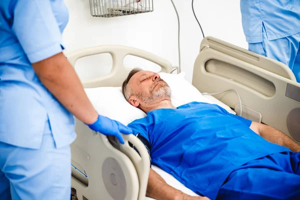Ein älterer Patient liegt auf einem Krankenhausbett. Uneinsichtiger Mann im Saal. blaue medizinische Kleidung. — Stockfoto