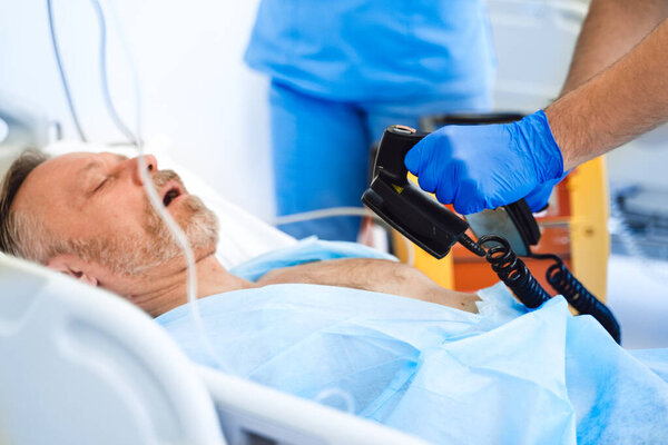 Доктор с дефибриллятором спасает жизнь пожилого человека. Скорая помощь. Первая помощь. Медики за работой
.