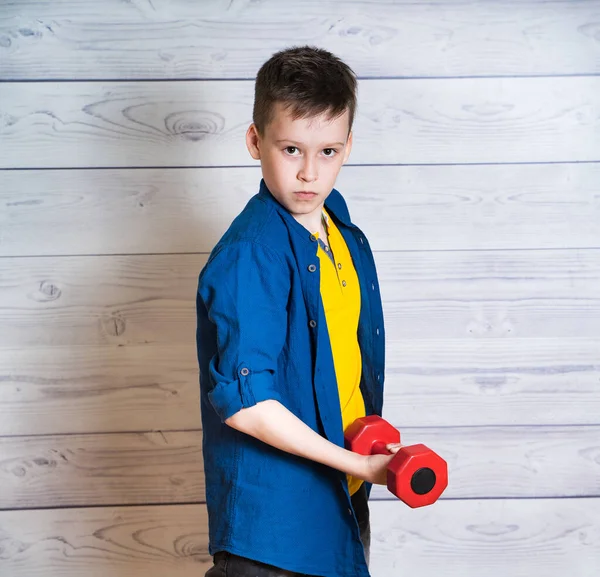 Portrait d'un garçon sérieux en T-shirt jaune et veste en denim, chemise. Petit garçon avec un haltère rouge. Portrait d'enfant adapté . — Photo