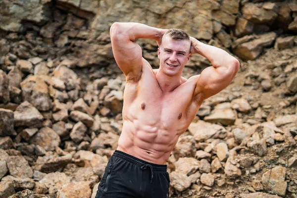 Fitness strongman posing with hands behind his head in a rocky background. Bodybuilder concept background - muscular bodybuilder handsome man pumping muscles. Half naked young men. Bare torso. — Stock Photo, Image