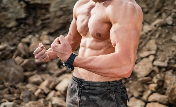 Fitness strongman posing with clenched fists in a rocky background. Bodybuilder concept background - muscular bodybuilder is pumping muscles. Half naked young men. Bare torso. Muscle hands closeup. — Stock Photo, Image