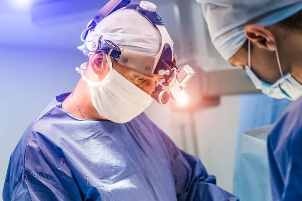A műtét folyamata orvosi felszereléssel. Két sebész a műtőben, sebészeti felszereléssel és távcsővel. Orvosi háttér. — Stock Fotó