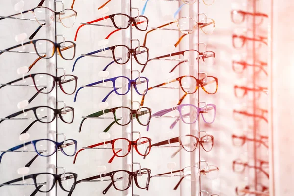Fila de gafas en una óptica. Tienda de anteojos. Soporte con gafas en la tienda de óptica. La mano de la mujer elige gafas. Corrección de la vista. — Foto de Stock