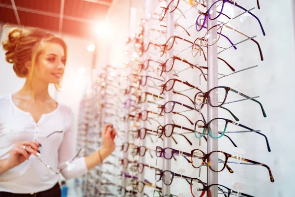 Fila di occhiali a un ottico. Negozio di occhiali. Stare con gli occhiali nel negozio di ottica. La donna sceglie gli occhiali. Correzione della vista. — Foto Stock