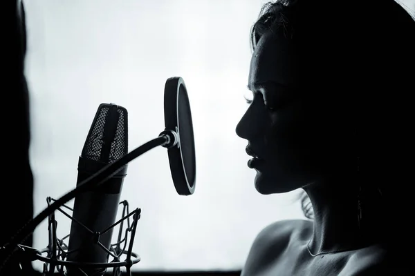 Jeune femme avec le micro dans le studio d'enregistrement. Enregistrement vocal professionnel. Photosession en noir et blanc. Belle chanteuse. Portrait. Gros plan . — Photo