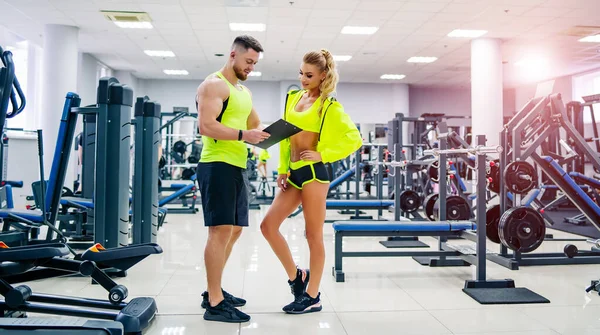 Picture of personal fitness trainer and female client in gym posing in front of the camera. Healthy life and fitness concept.