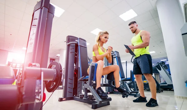 Personal handsome fitness trainer and beautiful blonde female client in gym making workout scedule. Healthy life concept. — Stock Photo, Image