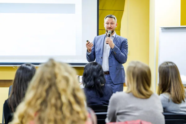 Positive young businessman doing a presentation to his colleagues. Handsome man with microphone. Young professional near the board. Selective focus. — ストック写真