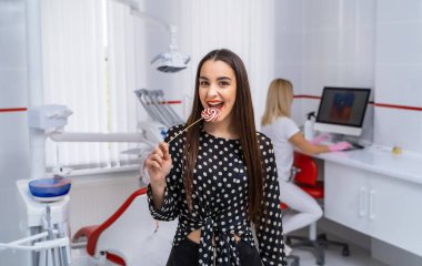 Neşeli gülümseyen kız ellerinin arasında bir şeker tutuyor. Diş hekimliği geçmişi. Yakın plan yatay fotoğraf.