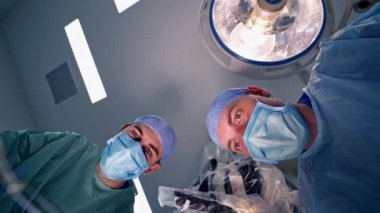 Maskeli iki doktorun portreleri. Tıbbi üniformalı profesyonel cerrahlar ameliyat yapıyor. Yakın plan. Aşağıdan görüntüle.