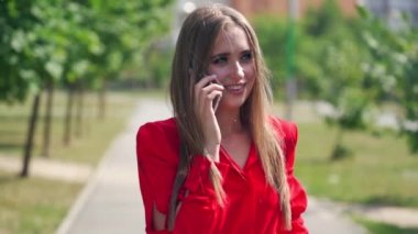 Genç bir kadın telefonda konuşuyor. Bulanık şehir arka planında cep telefonu tutan uzun saçlı güzel bir kadının portresi. Yavaş çekim.