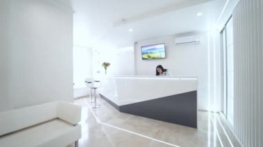 İçerideki stomatoloji merkezi. Resepsiyon masasında zarif bir bayan. Güzel bir kadın doktorun aramasını bekliyor. Kız bekleme odasındaki lüks koltukta oturuyor..