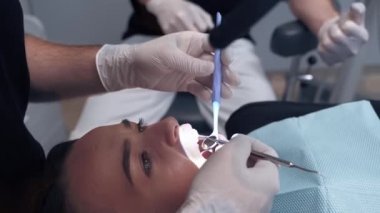 Diş hekimi hastanın dişlerini mikroskopla inceliyor. Uzman, dişçi muayenehanesinde dişinin ağzına tıbbi aletlerle bakıyor..