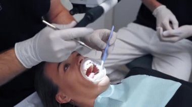 Dişçide ağzı açık olan yakın plan kadın yüzü. Eldivenli doktor hastanın dişlerini tıbbi aletlerle muayene eder. Diş hekimi kavramı.