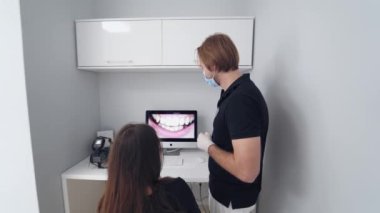 Stomatolog bir kadına danışmanlık yapıyor. Doktor genç hastaya dişlerinin durumunu gösteriyor. Diş hekimi, dişçi muayenehanesindeki ekranda kadın dişlerinin fotoğrafını gösteriyor..