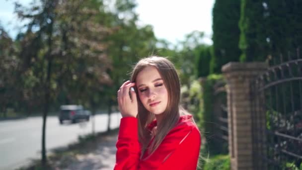 穿着红色衣服的可爱的女孩 漂亮的年轻模特儿站在室外 在镜头前摆姿势 绿树背景上一个漂亮女人的画像 — 图库视频影像