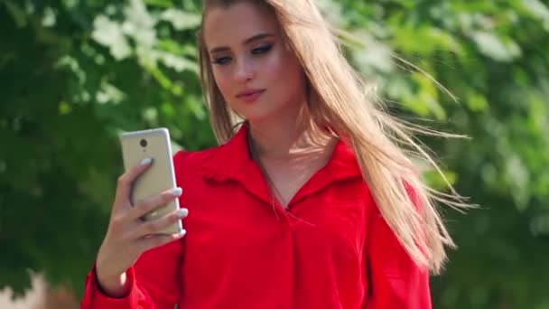Belle femme qui fait du selfie. Magnifique jeune femme en robe rouge se photographiant sur le téléphone portable à l'extérieur.