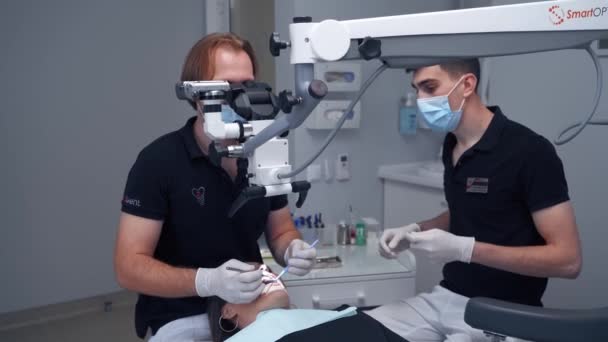 歯科医は現代的な装置を使う 歯科室で顕微鏡を通して患者の歯を治療する専門医 専門医と診療所の助手 — ストック動画