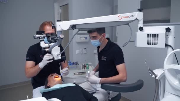 彼の助手と男性歯科医は患者の歯を治療する 歯科の近代的な技術 組織学者は顕微鏡を通して女性の口を調べる — ストック動画