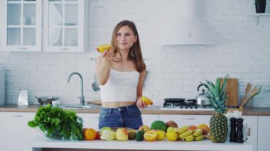 Mutfakta güzel bir kadın var. Gülümseyen genç bir kadın taze portakal teklif ediyor. Sağlıklı organik meyve ve sebzeler masada..