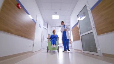 Tekerlekli sandalyedeki hasta doktorla konuşuyor. Hemşire, modern kliniğin koridorunda tekerlekli sandalyeli bir kadını itiyor. Hastane koridoru.