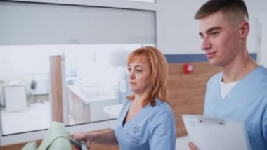 Doktor ve asistanı klinikte. Koridorda hasta bir hastayla tekerlekli sandalye iten kadın hemşire. Hastane koridorundaki sağlık çalışanlarının arka görüntüsü..