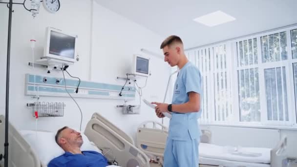 Jovem Médico Falar Com Doente Homem Sênior Deitado Cama Hospital — Vídeo de Stock