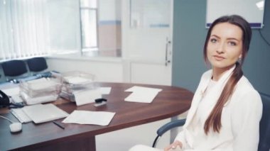 Kamerada konuşan kadın doktorun portresi. Masada oturan güzel doktor kadın modern klinikteki bir erkek uzmanla konuşuyor..