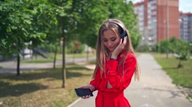 Açık havada müzik dinleyen çekici bir kadın. Kulaklıklı kırmızı elbiseli genç bir bayan yazın şehir caddesinde müzik dinlemekten hoşlanır..