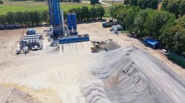 Yukarıdan asfalt bitkisi. Kazıcı dışarıdaki yığının üzerine harabeler döker. Asfalt fabrikasının modern toprakları doğayla çevrili..