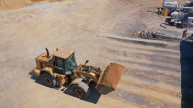 Asfalt arazisindeki kazıcı açık havada üretiyor. Modern kazıcı kovadan özel bir tanka kum döküyor. Üst görünüm.