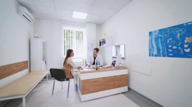 Genç bir kadın bir doktorla sohbet ediyor. Erkek doktor, klinikte modern ofis geçmişi olan bir kadınla konuşuyor. Tıbbi bakım konsepti.