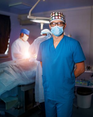 Maskeli ve gözlüklü doktorun portresi. Ameliyathanede ameliyat ekipmanlarıyla bir grup cerrah. Tıbbi geçmişi var. Seçici odak
