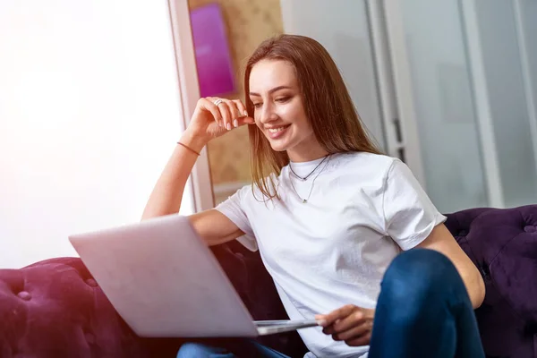 Woman in living room sitting on sofa using laptop. Smiling young beautiful girl.