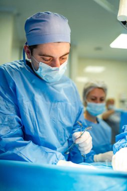 Maskeli doktor, önlük ve lateks eldiven. Cerrahlar arka planda parlak modern cerrahi odasında cerrahi operasyon yapıyorlar. Ameliyathane. Klinikte modern ekipmanlar. Acil Servis..